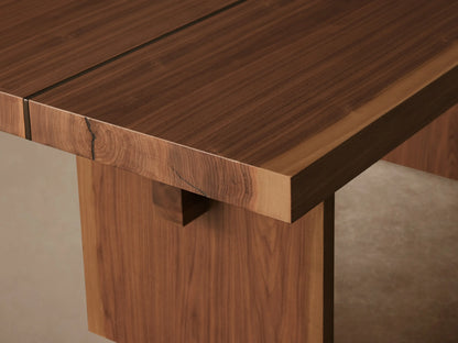 Mihaela Dining Table in a Walnut finish, featuring a rectangular top with visible wood grain, supported by two parallel plank legs and a horizontal crossbar.