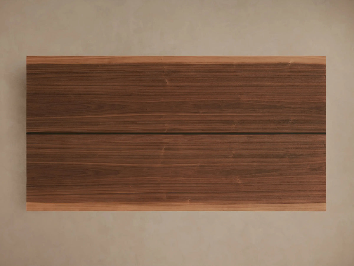 Mihaela Dining Table corner with American walnut veneer, showcasing a smooth wood grain and hand-carved detailing, placed on a light surface.