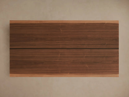 Mihaela Dining Table corner with American walnut veneer, showcasing a smooth wood grain and hand-carved detailing, placed on a light surface.