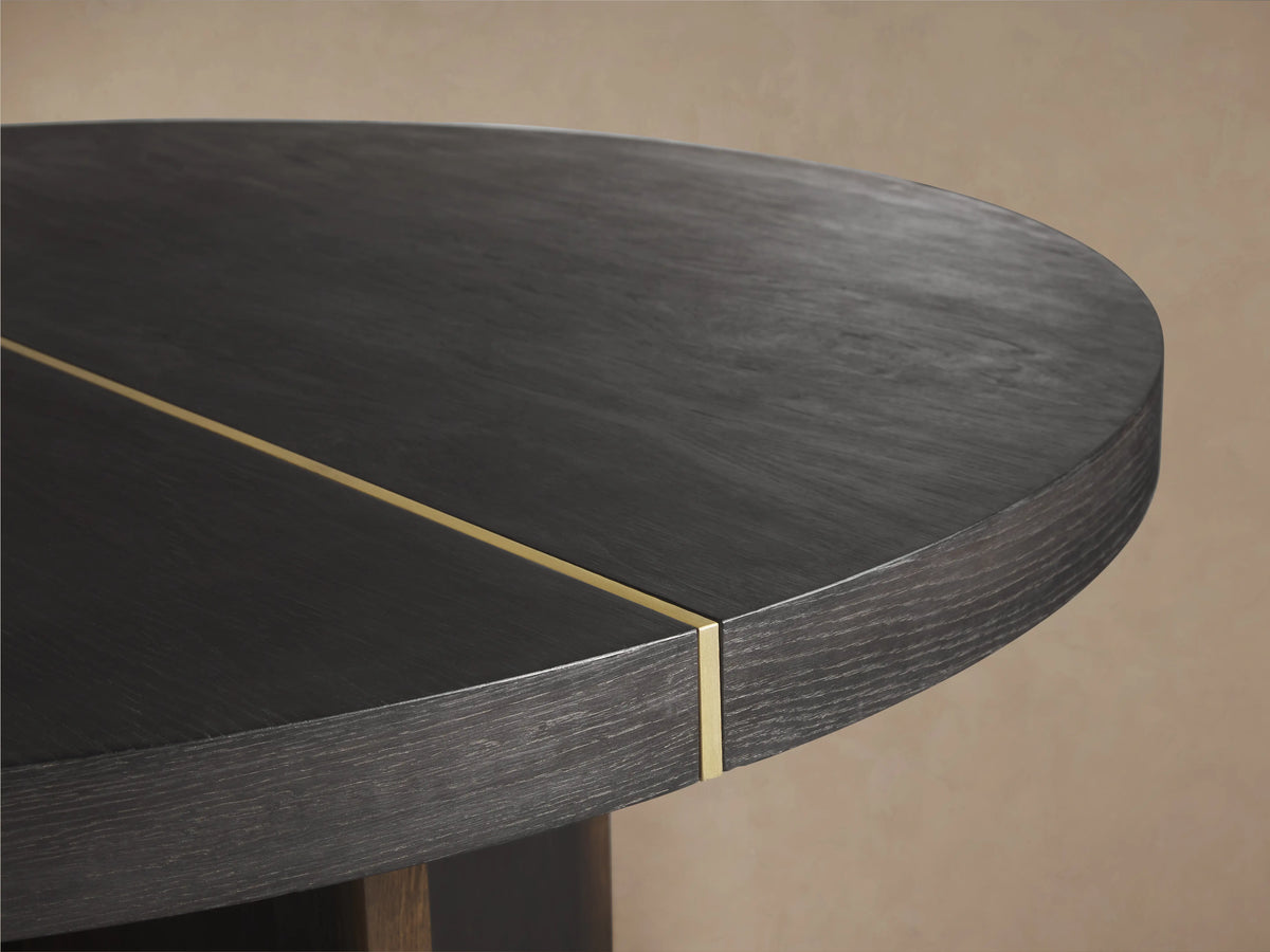 Mihaela Round Dining Table, dark wood with visible grain & brass accent line. Angled view of round top & cross-shaped base.