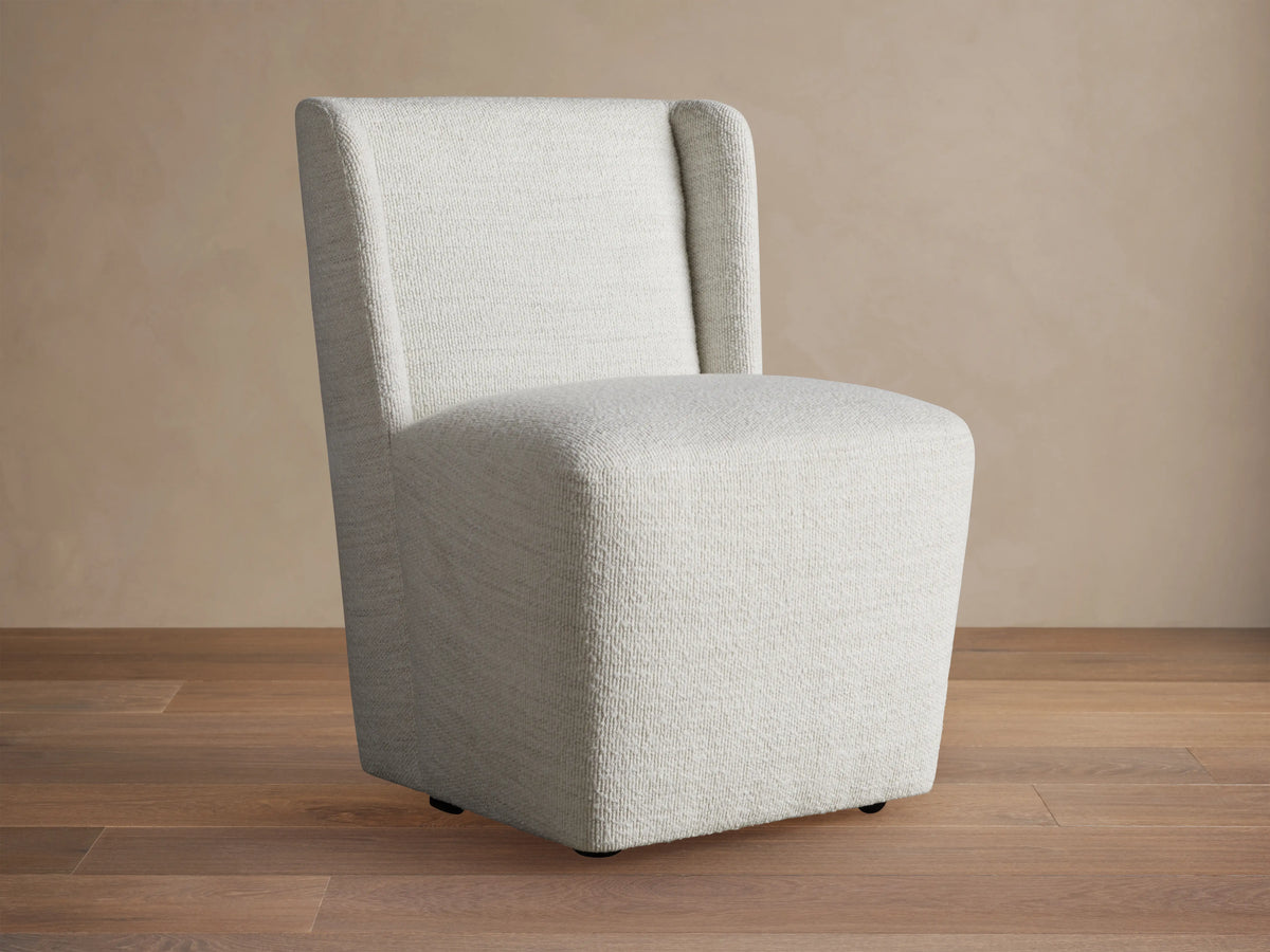 Mila Dining Chair with light beige fabric, featuring a sleek, armless design and subtle texture on wooden floor.