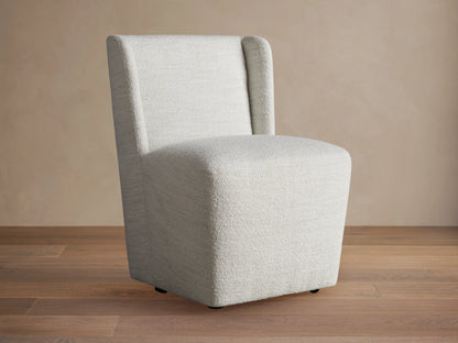 Mila Dining Chair with light beige fabric, featuring a sleek, armless design and subtle texture on wooden floor.