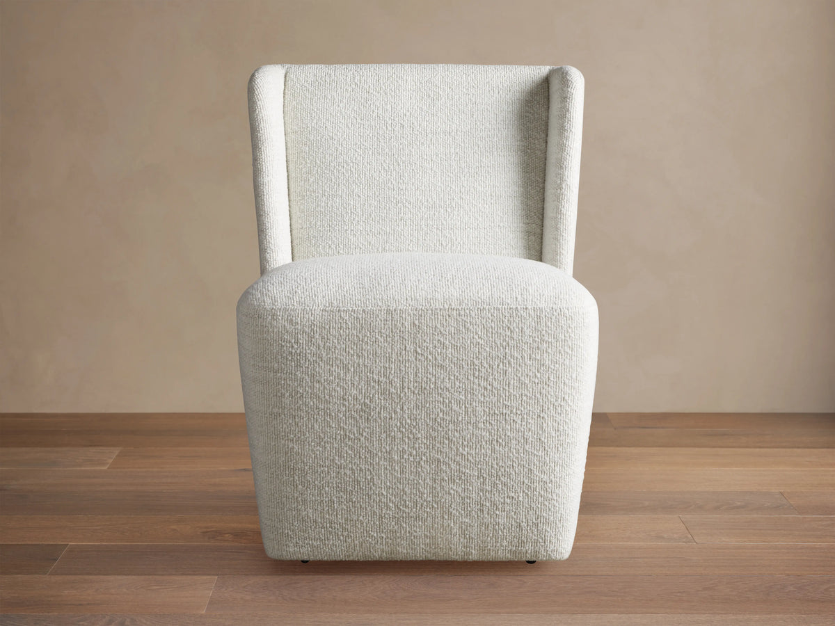 Mila Dining Chair with light beige fabric, featuring a sleek, armless design and subtle texture on wooden floor.