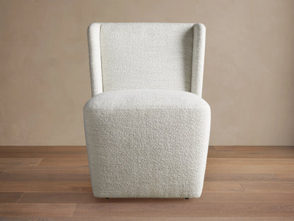Mila Dining Chair with light beige fabric, featuring a sleek, armless design and subtle texture on wooden floor.