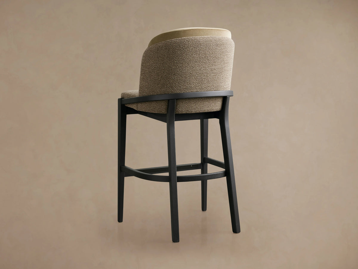 Mena Stool with beige faux leather upholstered back and taupe seat on a solid black ash wood frame, placed on wooden flooring.