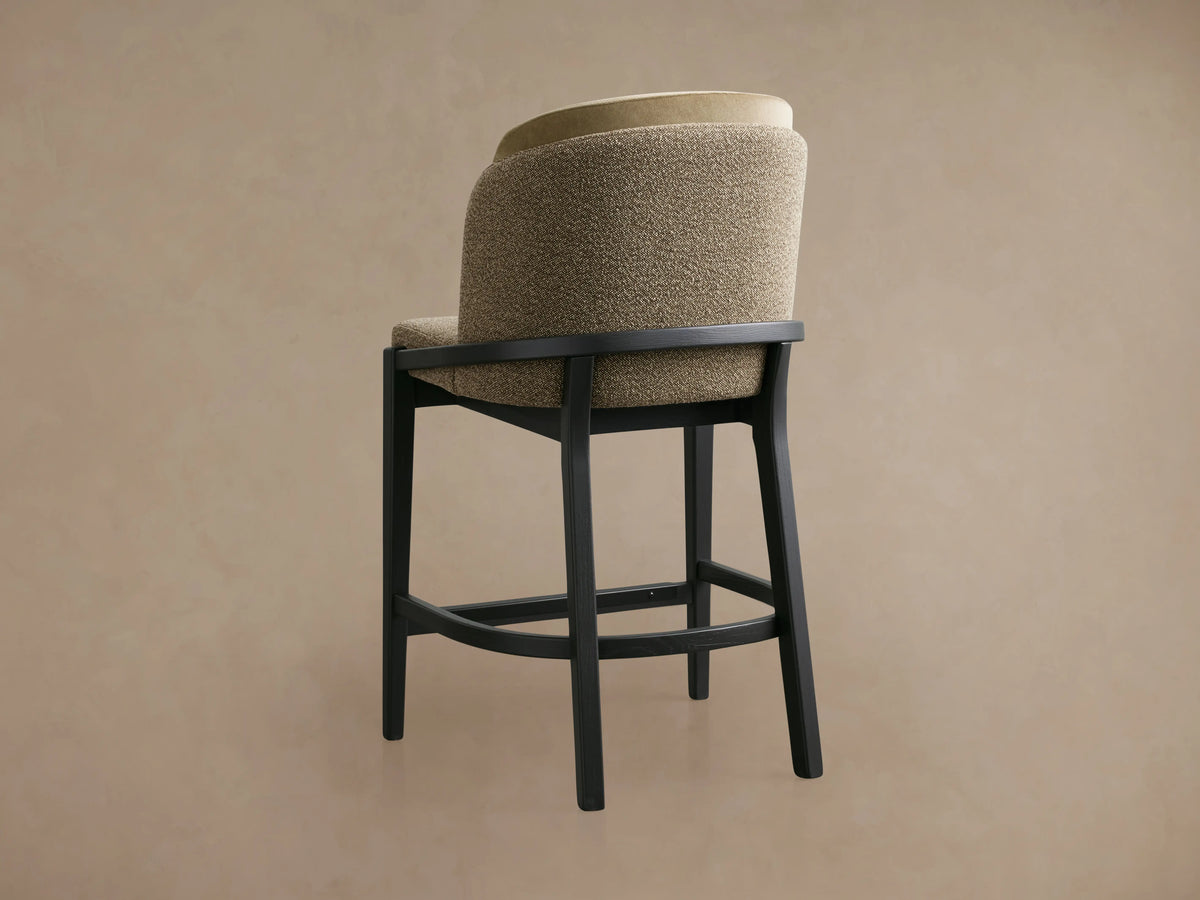 Mena Stool with beige faux leather backrest, taupe fabric seat, and black ash wood frame on wooden floor.
