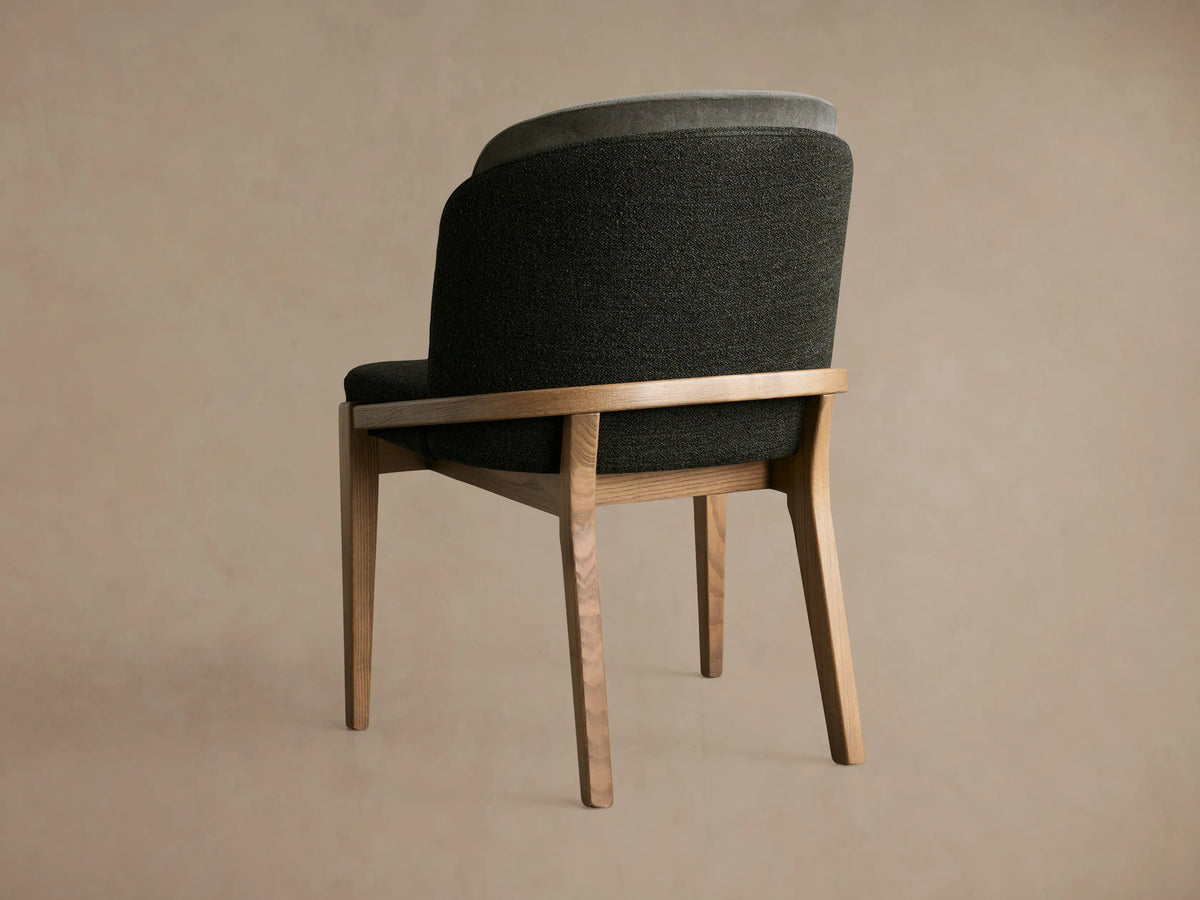 Angled back view of a Mena Dining Chair with an ash wood frame, dark gray and light gray layered fabric back, and tapered legs.