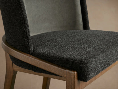 Angled view of Mena Dining Chair: dark gray fabric seat, lighter gray inner back, brown ash wood frame, tapered legs.