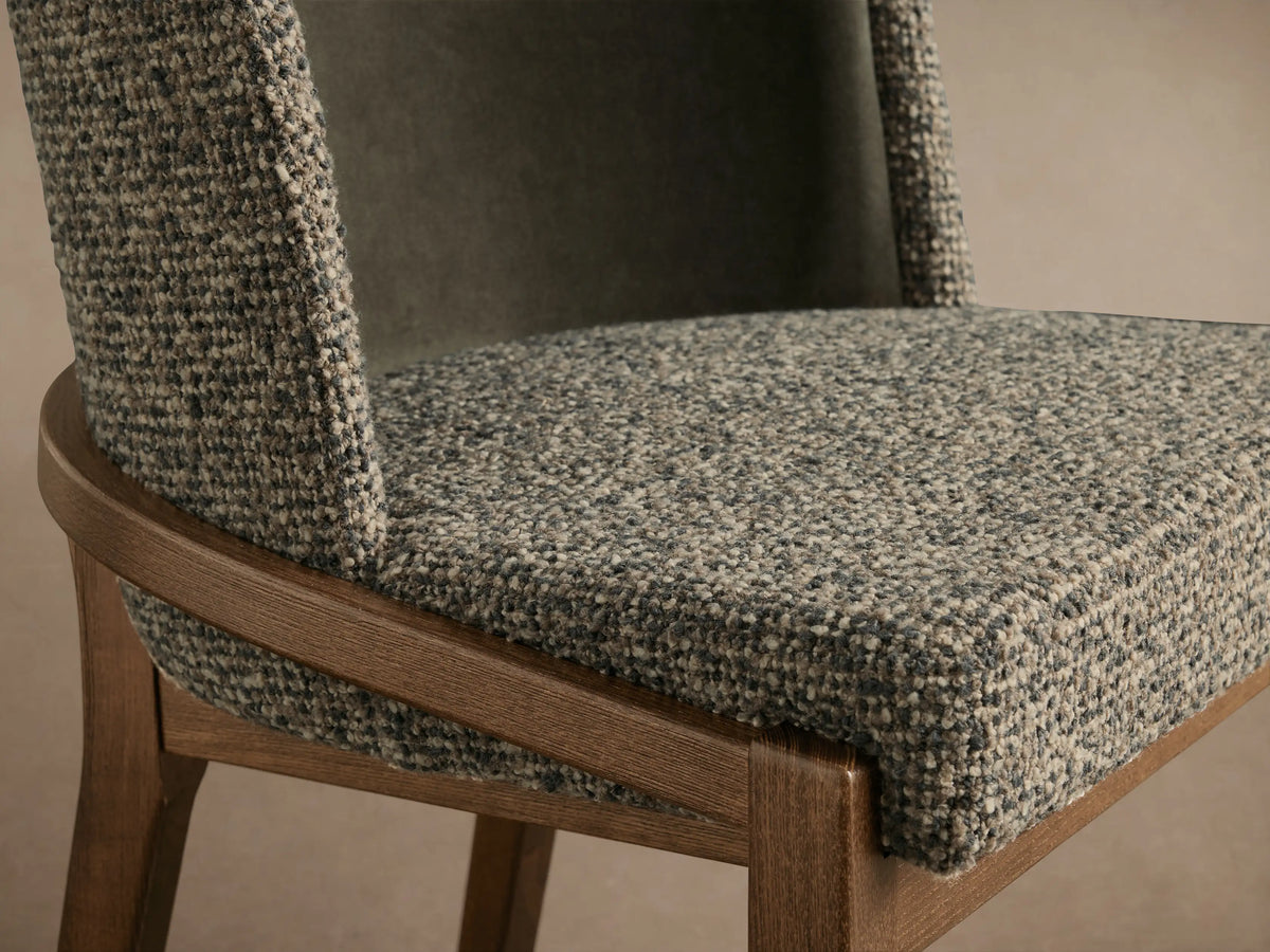 Mena Dining Chair, angled close-up. Light gray textured fabric seat & outer back, dark green inner back, and curved ash wood frame.
