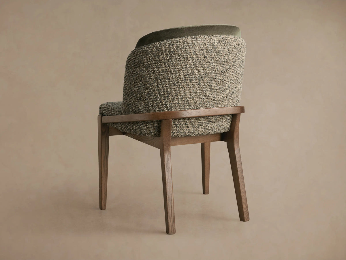 Mena Dining Chair, angled back view. Ash wood frame, layered back with textured green/beige fabric & dark green velvet trim.
