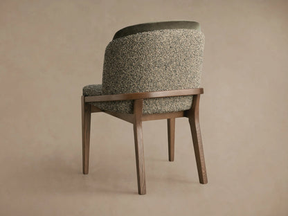 Mena Dining Chair, angled back view. Ash wood frame, layered back with textured green/beige fabric & dark green velvet trim.