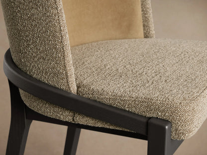 Modern chair with curved mustard fabric back, textured beige seat, and dark wood frame. Centered on a wooden floor.