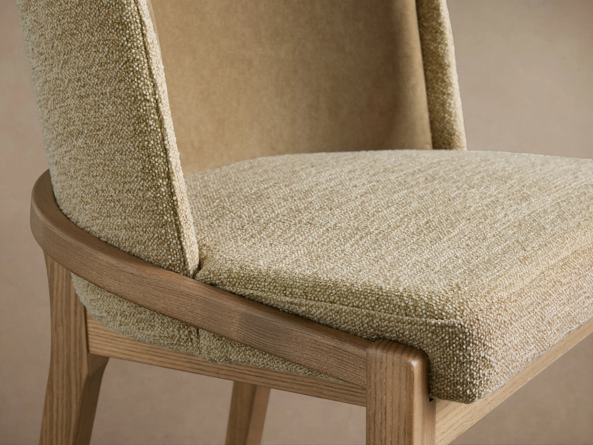 Close-up of Mena Dining Chair. Light beige textured fabric seat, darker smooth backrest, and light ash wood frame.