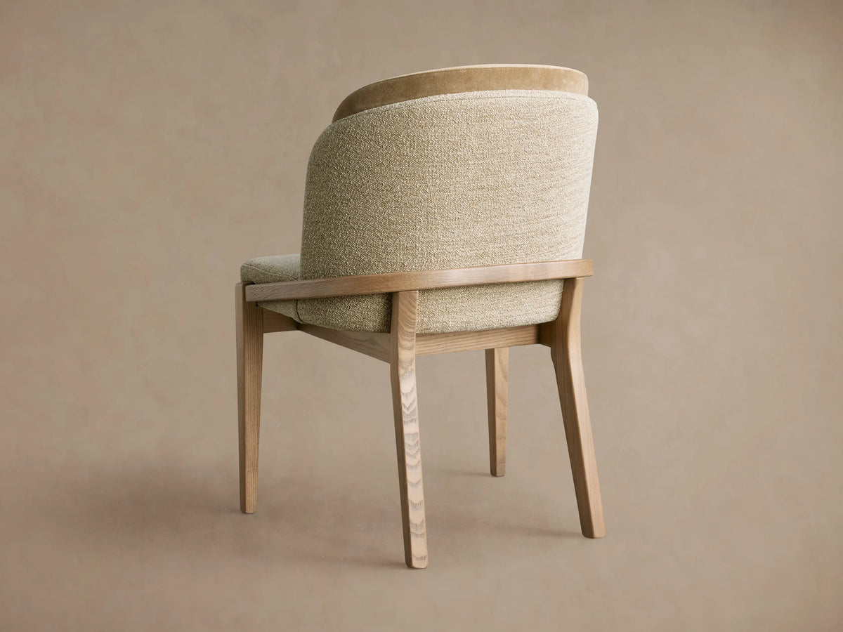 Angled Mena Dining Chair, back-left view. Light ash wood frame, textured light beige/green & smooth tan upholstered back.