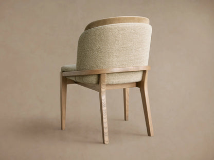 Angled Mena Dining Chair, back-left view. Light ash wood frame, textured light beige/green & smooth tan upholstered back.
