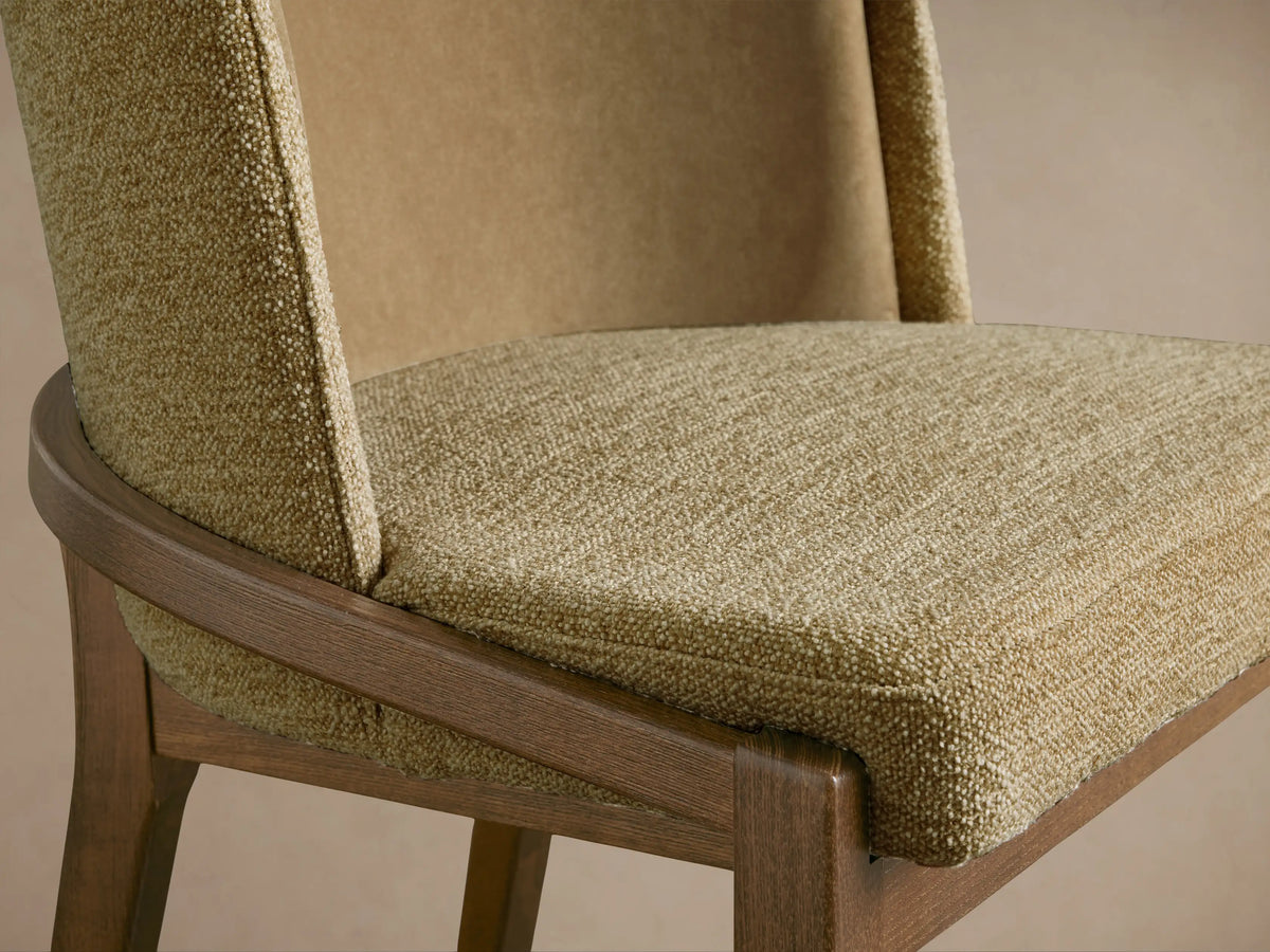 Close-up of Mena Dining Chair's light brown textured fabric seat, layered backrest, and curved dark wood frame.