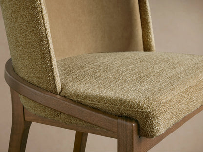 Close-up of Mena Dining Chair's light brown textured fabric seat, layered backrest, and curved dark wood frame.