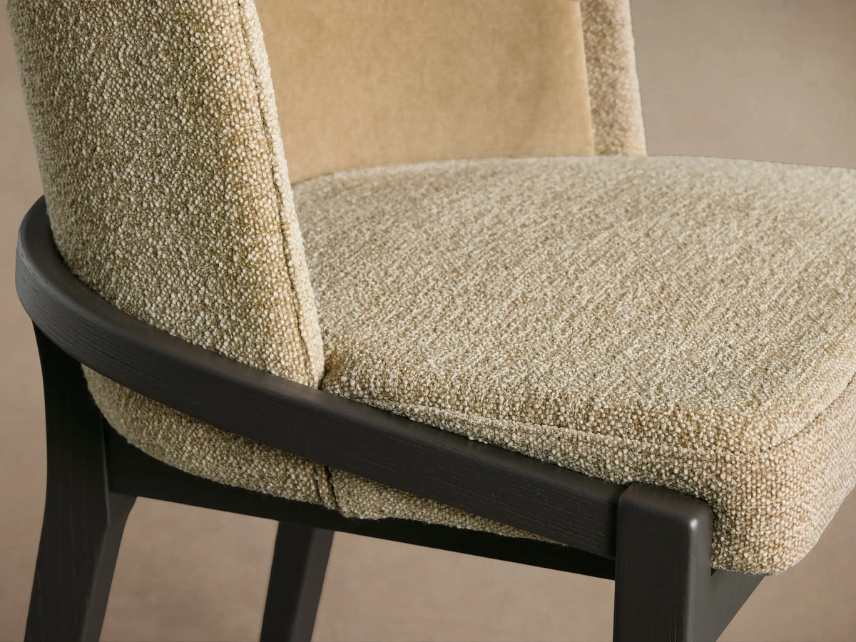 Mena Dining Chair close-up. Light beige textured fabric seat, two-tone back, dark ash wood frame with curved arm.