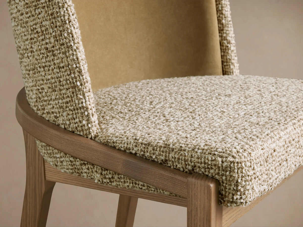 Close-up of Mena Dining Chair. Features a curved ash wood frame, textured cream/beige seat, and smooth tan inner backrest.
