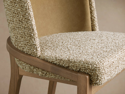Close-up of Mena Dining Chair. Features a curved ash wood frame, textured cream/beige seat, and smooth tan inner backrest.