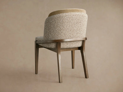 Mena Dining Chair, angled back view. Dark ash wood frame, tapered legs. Layered backrest with light beige textured and smooth fabrics.