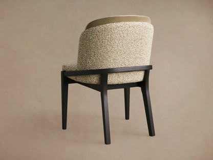 Mena Dining Chair, angled back view. Dark wood frame, textured beige upholstery with a lighter olive top back accent, curved back.
