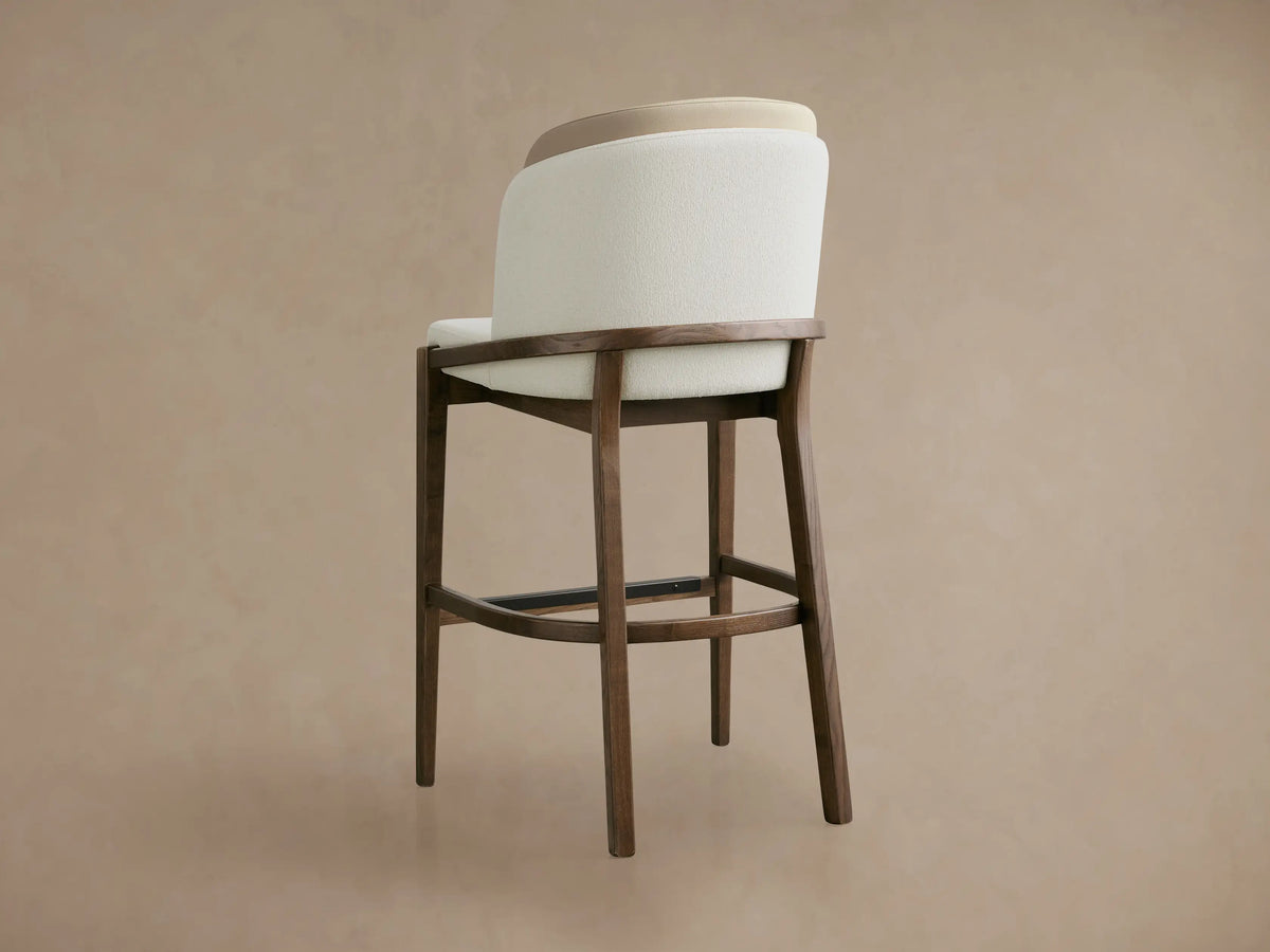 Angled close-up of Mena Stool, featuring a cream textured fabric seat, layered backrest, and dark ash wood frame.