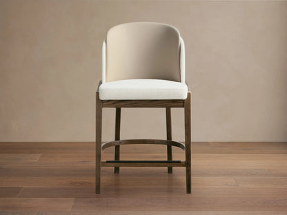 Mena Stool, dark ash wood frame with tapered legs, light cream upholstered seat & two-tone beige backrest, on wood floor.