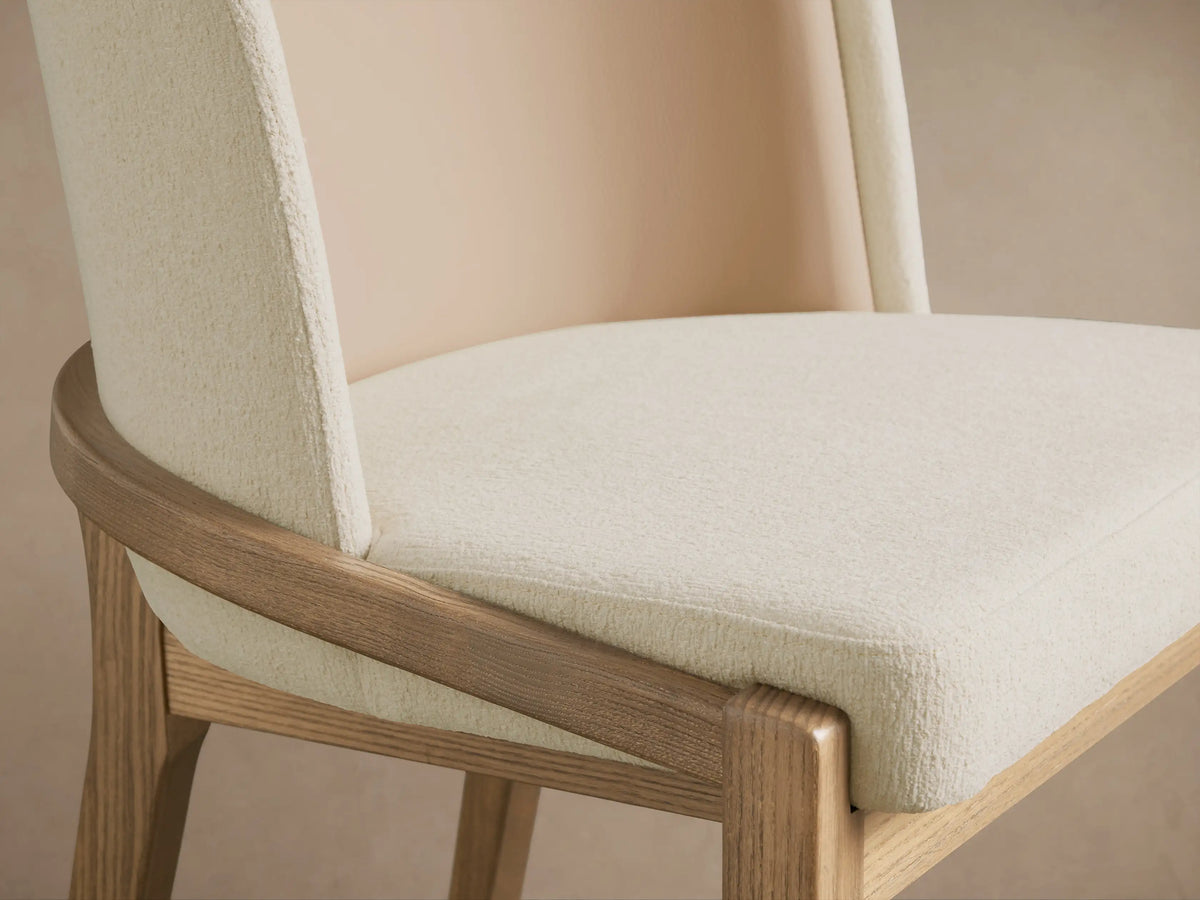 Mena Dining Chair, close-up. Light ash wood frame with curved rail, cream textured fabric seat and outer back, tan inner back.