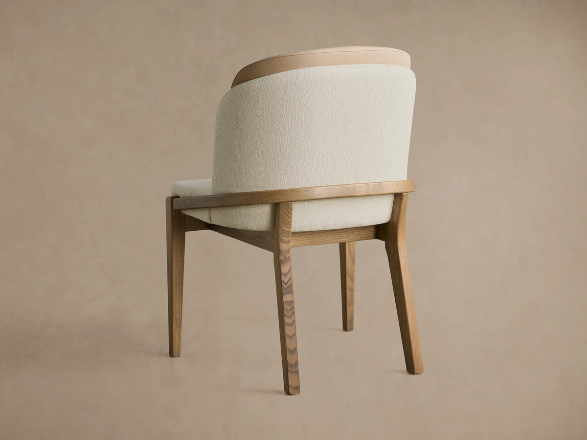 Mena Dining Chair, 3/4 back view. Cream fabric & light brown leather layered back, ash wood frame, tapered legs.