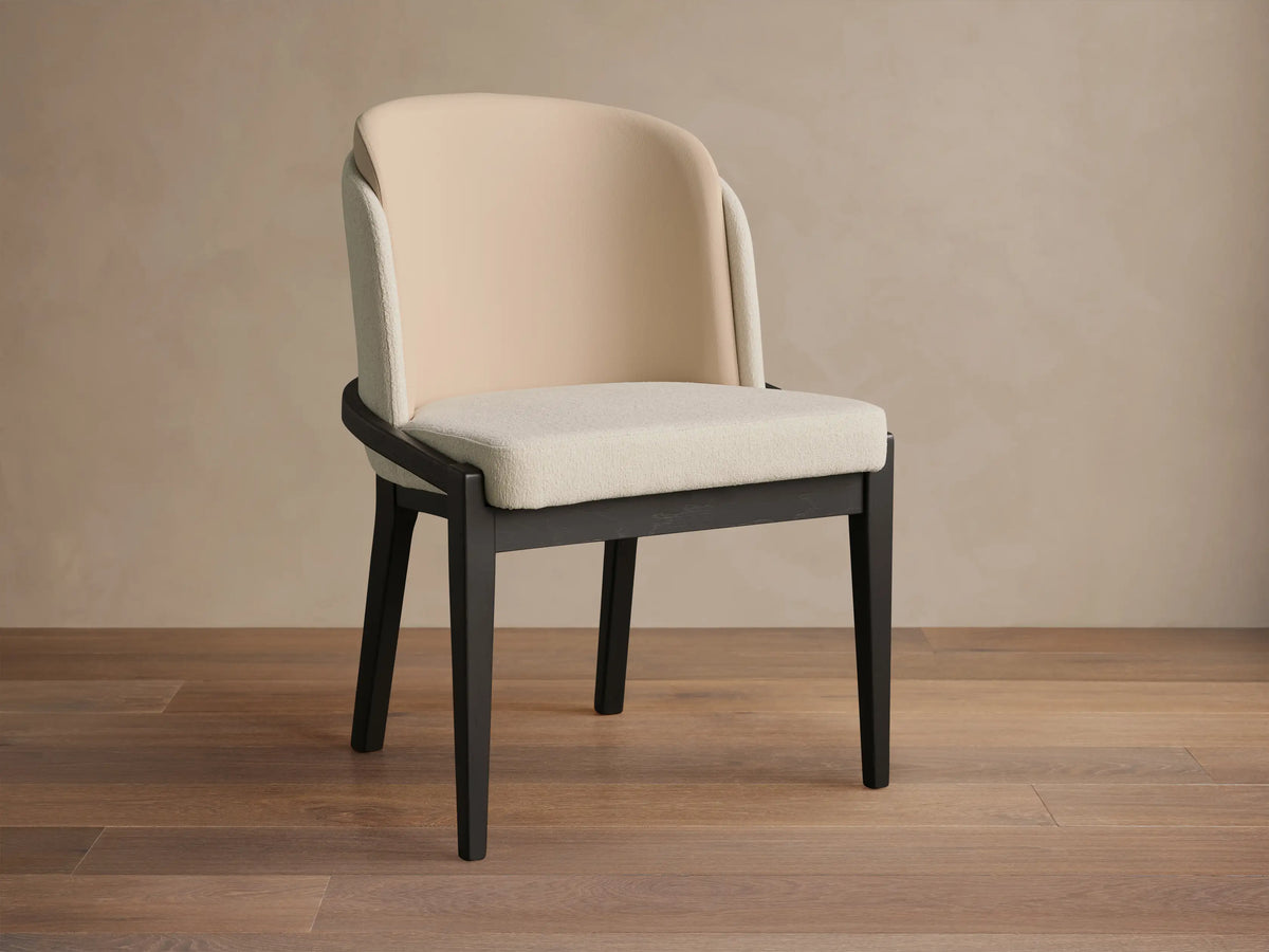 Mena Dining Chair: Dark ash frame with layered beige fabric backrest and light cream seat, angled on a wood floor.