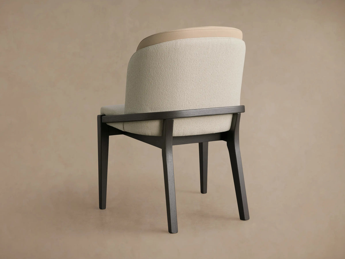 Close-up of Mena Dining Chair's textured cream seat & layered backrest, with a curved dark ash wood frame and tapered leg.