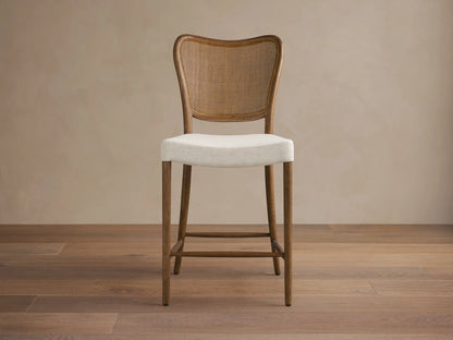 Noa Stool, cinder-stained oak frame, woven rattan back, light cream fabric cushion, angled right on wood floor.