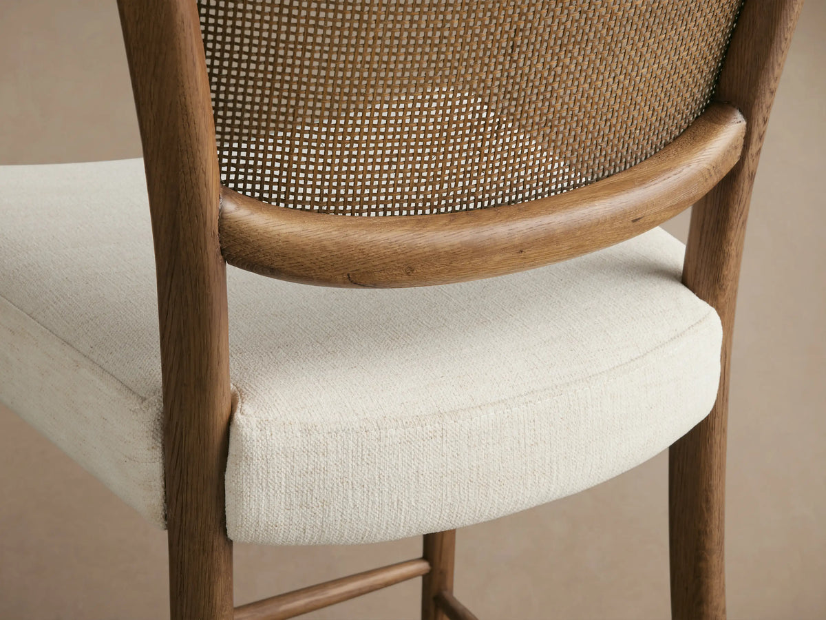Noa Stool with Cinder-finished oak frame, woven rattan backrest, and light beige upholstered seat, front view.