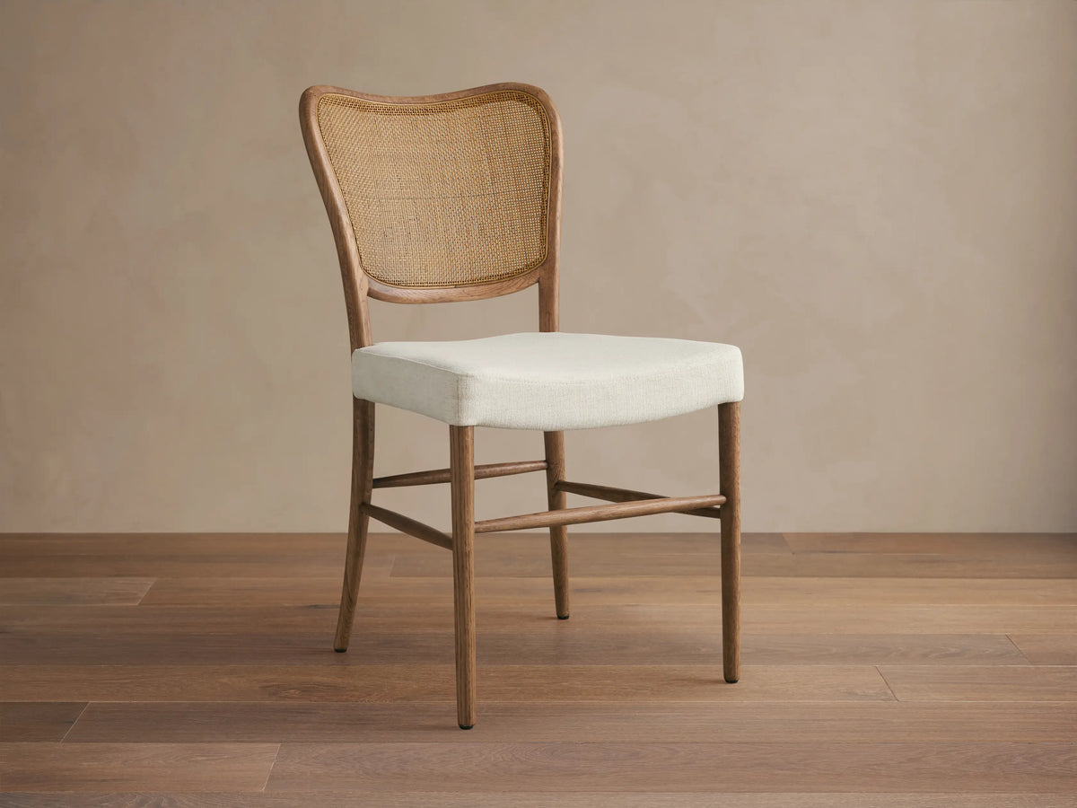 Noa Dining Chair with medium brown oak frame, curved woven rattan back, and cream fabric seat, viewed from front.