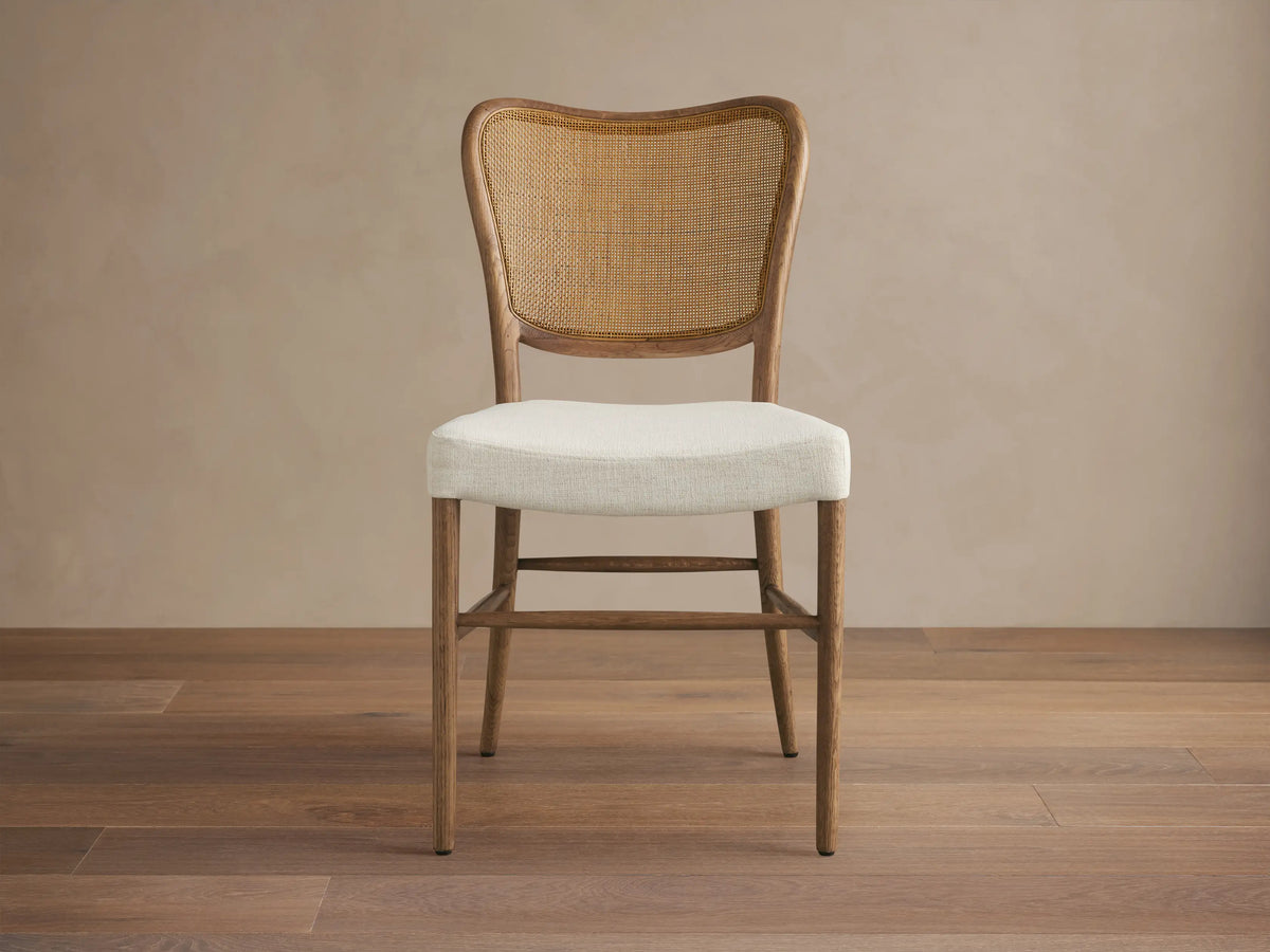 Noa Dining Chair with medium brown oak frame, curved woven rattan back, and cream fabric seat, viewed from front.