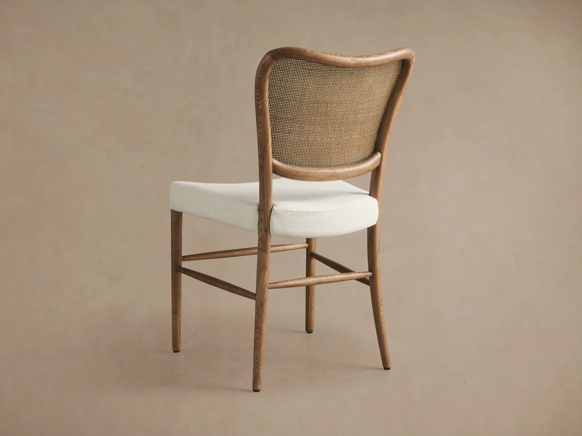 Angled close-up of Noa Dining Chair, showing light oak frame, curved woven rattan backrest, and cream fabric seat.