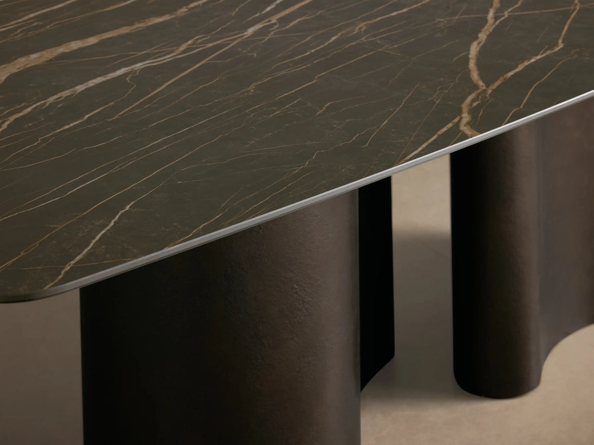 Front-side view of the Ortenzia Dining Table with a dark ceramic tabletop featuring light marble veining and a wavy steel base.