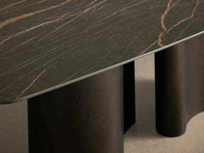 Front-side view of the Ortenzia Dining Table with a dark ceramic tabletop featuring light marble veining and a wavy steel base.