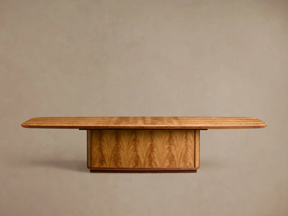 Front view of the Palma Extension Dining Table, featuring a light brown wood veneer tabletop with rounded corners and a pedestal base with arched graining.