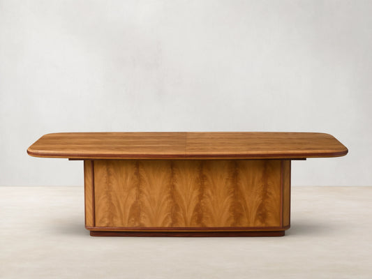 Front view of the Palma Extension Dining Table, featuring a light brown wood veneer tabletop with rounded corners and a pedestal base with arched graining.