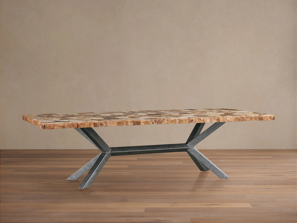 Petra Dining Table with a textured petrified wood surface and solid iron legs in a dark grey patina, set on a wooden floor.
