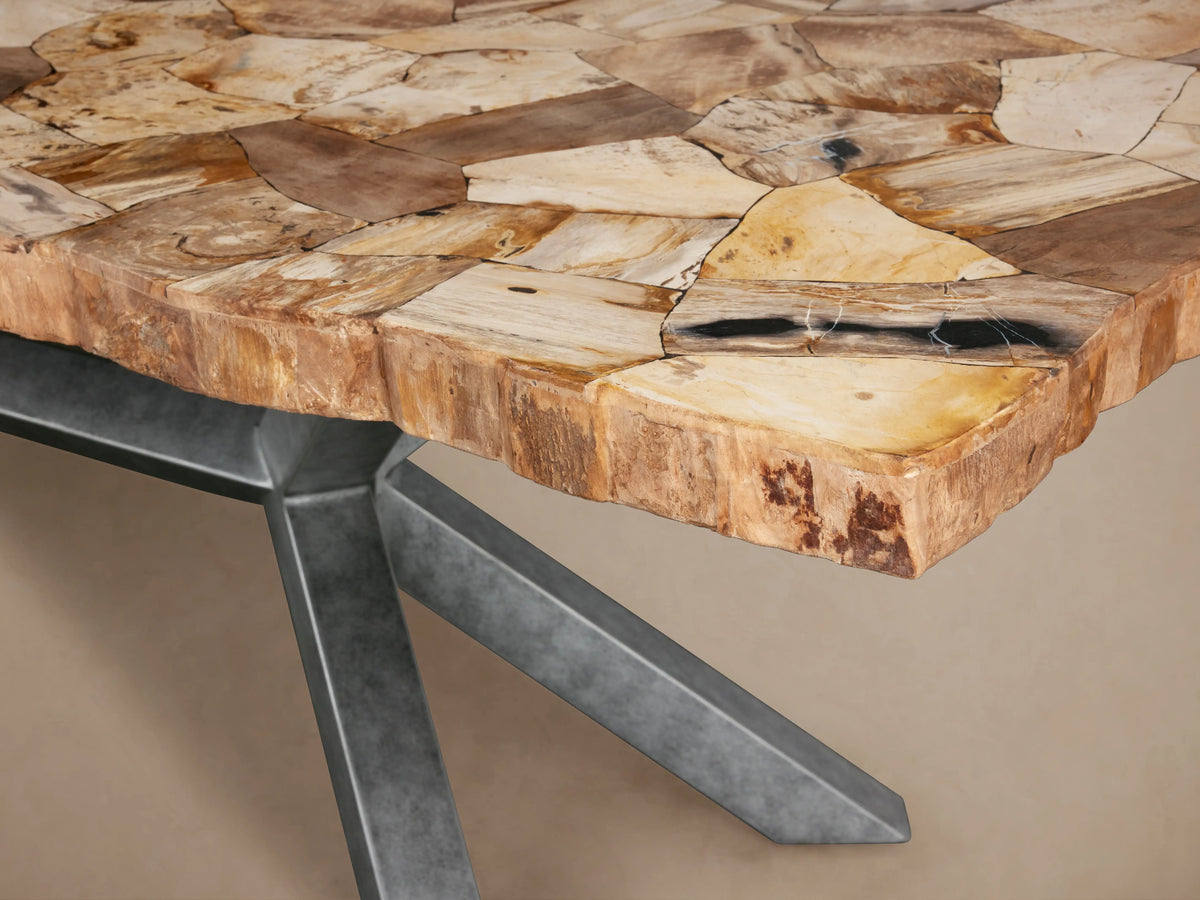 Petra Dining Table with a natural stone top showcasing varied earth tones, set on a dark grey iron base with an X-shaped design, on wooden floor.