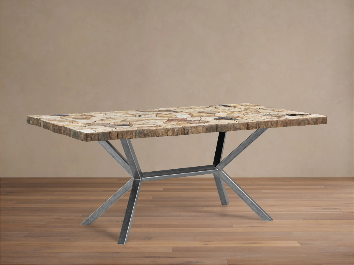 Petra Dining Table with a petrified wood top showing natural variations, supported by a V-shaped iron base with dark grey patina.