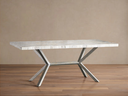 Rectangular Petra Dining Table with a textured grey stone top and crossed iron legs, featuring an antiqued dark grey patina, on a wooden floor.