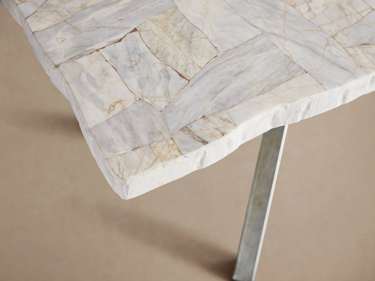Rectangular Petra Dining Table with light stone surface and dark grey iron X-shaped legs on wooden floor.