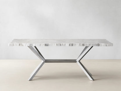 Rectangular Petra Dining Table with a textured grey stone top and crossed iron legs, featuring an antiqued dark grey patina, on a wooden floor.