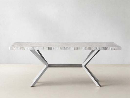 Rectangular Petra Dining Table with a textured grey stone top and crossed iron legs, featuring an antiqued dark grey patina, on a wooden floor.