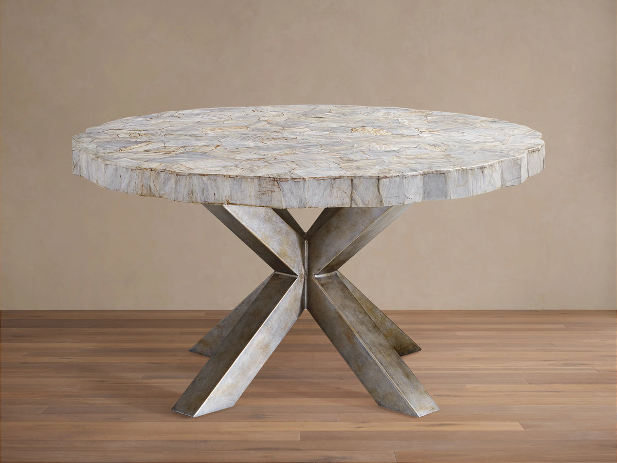 Round dining table with petrified wood top and textured surface, supported by an X-shaped iron base with dark grey patina, on wood floor.