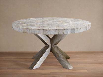 Round dining table with petrified wood top and textured surface, supported by an X-shaped iron base with dark grey patina, on wood floor.
